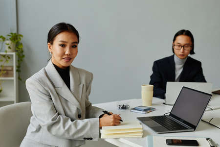 Portrait of young Asian businesswoman looking at camera and smiling while working at table in minimal modern officeの写真素材