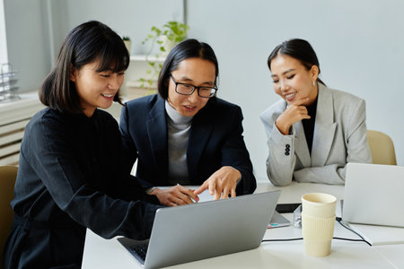 Portrait of Asian business team of three people looking at laptop screen and smiling while meeting in officeの写真素材