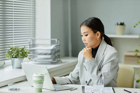 Minimal portrait of beautiful Asian woman using laptop while working in office at deskの写真素材