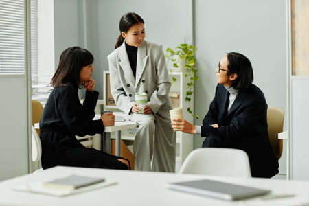 Group of young Asian business people chatting during coffee break in office interiorの写真素材