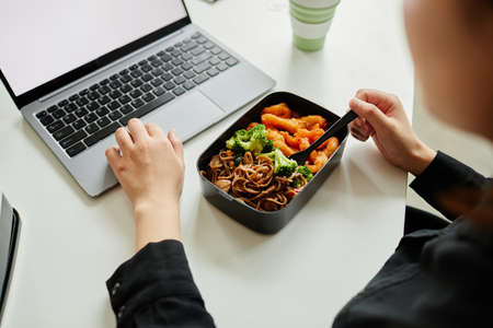 Close up of young woman enjoying healthy lunch with vegetables while using laptop, copy spaceの写真素材