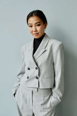 Vertical waist up portrait of beautiful Asian businesswoman wearing suit and looking at camera