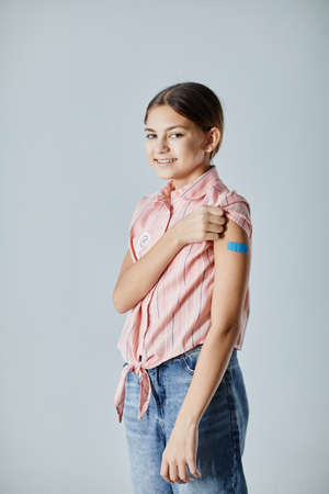 Vertical portrait of cute teenage girl showing shoulder patch and smiling at camera after getting...