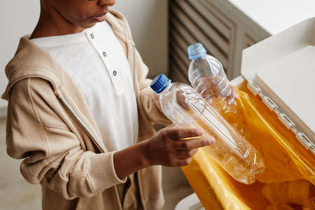 Cropped shot of African-American boy putting plastic in recycling bins at home, copy spaceの写真素材