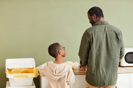 Minimal back view portrait of African-American father and son sorting household waste at home, copy spaceの写真素材