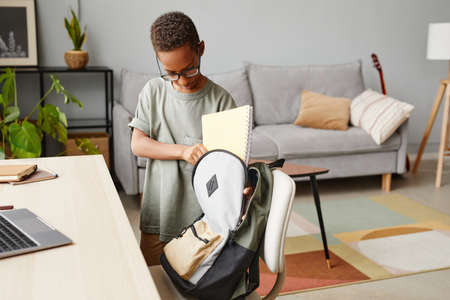 Portrait of young African-American boy packing backpack at home, copy spaceの写真素材