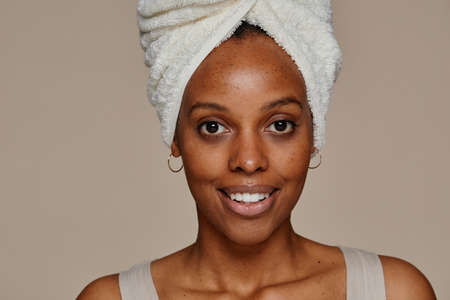 Minimal close up portrait of young African-American woman wearing head towel looking at camera while standing against neutral backgroundの写真素材
