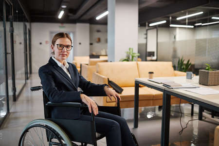 Portrait of successful businesswoman using wheelchair and looking at camera smiling while posing in...