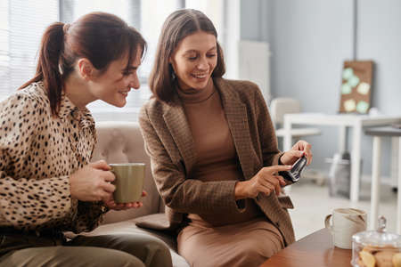 Happy pregnant woman showing the scan of her baby to her colleague while they drinking coffee during...