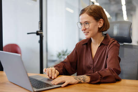 Portrait of smiling young woman using laptop while working in personal office, copy space