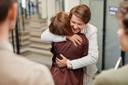 Portrait of smiling female manager embracing employee while celebrating promotion in officeの写真素材