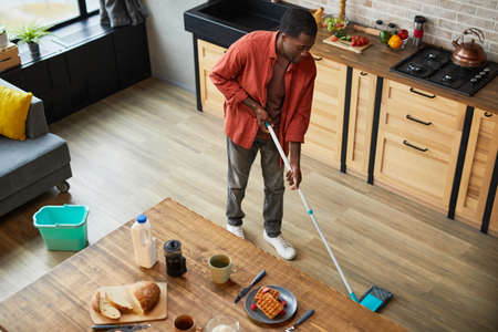 High angle portrait of young African-American man mopping floors while cleaning cozy apartment, copy spaceの写真素材