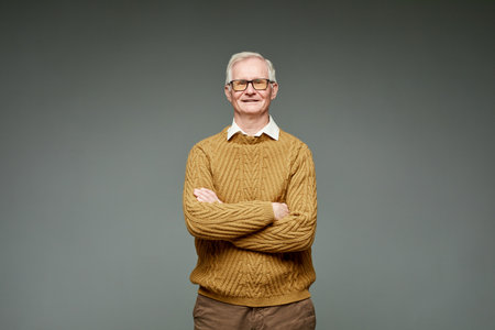 Contemporary aged grey-haired businessman in knitted brown sweater keeping crossed arms by his chest...