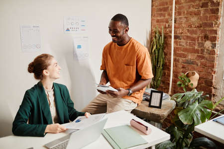 Two young contemporary intercultural male and female brokers in casual clothes having discussion of...