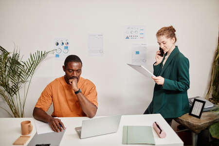 Young serious African American businessman looking at laptop screen while his Caucasian female...