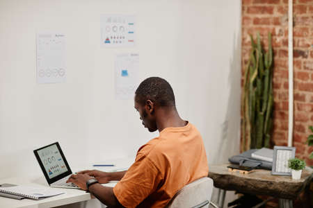 Contemporary young male economist analyzing financial data on lapto pscreen while sitting by desk in openspace officeの写真素材