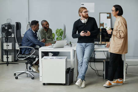 Young contemporary program managers talking at break while their two colleagues working in front of computer in officeの写真素材