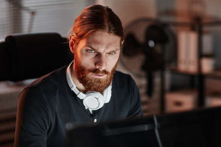 Young contemporary businessman or programmer looking through online data while working late in front of computer in officeの写真素材