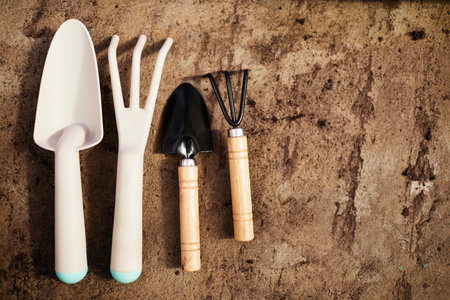 Two pairs of garden shovel and fork made up of white plastic, wood and black metal on shabby brown backgroundの写真素材