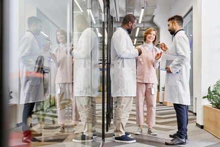 Two intercultural male healthcare workers and their female colleague having talk in corridor of contemporary medical centerの写真素材