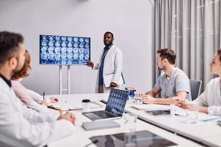 Group of young healthcare workers in lab coats looking at speaker pointing at medical scan of human brain during presentationの写真素材
