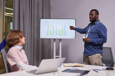 Contemporary confident medical expert pointing at interactive screen with charts while analyzing data during presentation at seminarの写真素材