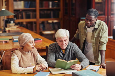Portrait of white haired senior man studying in library with two young studentsの写真素材