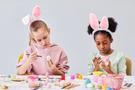 Minimal portrait of two girls painting Easter eggs and wearing bunny ears at art and craft class in school, copy spaceの写真素材