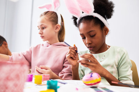 Children painting Easter eggs and wearing bunny ears while enjoying art and craft class in school