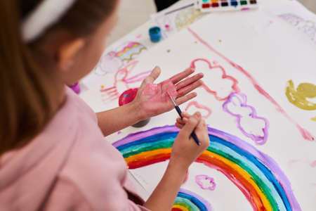 Close up of little girl drawing rainbow while enjoying finger painting at Easter party for children, copy spaceの写真素材