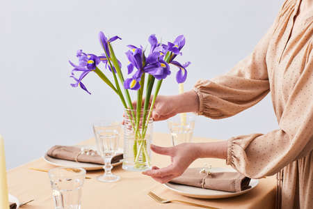 Minimal close up of young woman decorating dinner table with elegant Iris flowers for Spring, copy...