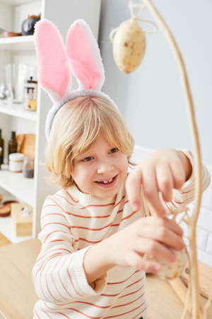 Vertical portrait of cute little boy playing games on Easter indoors and wearing bunny ears