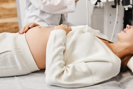 Close up of pregnant young woman preparing for ultrasound in medical clinic with focus on belly