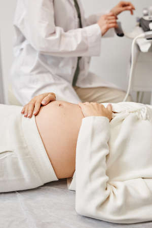 Vertical closeup of pregnant young woman preparing for ultrasound in medical clinic with focus on...