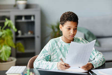 Portrait of African American teenage girl holding test sheet while studying at home, copy spaceの写真素材