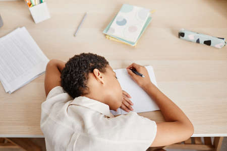Minimal top view of bored African American girl laying head on desk while struggling with homework