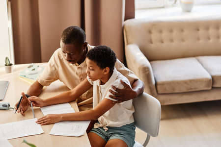 Warm toned portrait of teenage girl doing homework with father while preparing for school tests