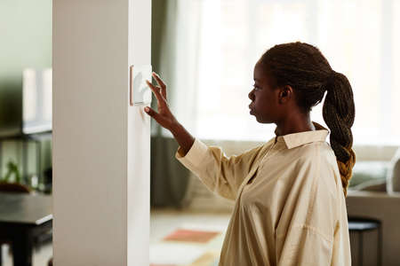 Minimal side view portrait of African American woman using smart home control panel in modern interior, copy spaceの写真素材