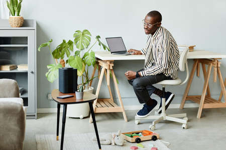 Full length portrait of African American man using voice activated smart speaker in minimal home...