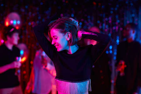Waist up portrait of carefree young woman dancing at party in neon lights, copy spaceの写真素材