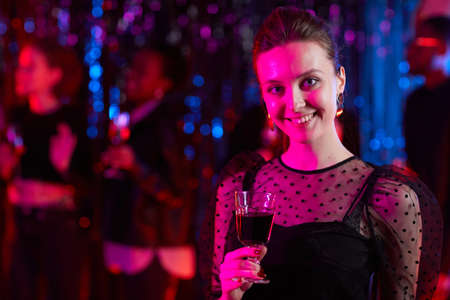 Portrait of young woman partying and holding drink in neon lights, copy space