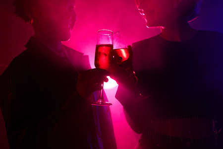 Backlit portrait of two young women enjoying drink while partying in smoky club with neon lights, copy spaceの写真素材