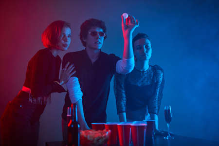 Portrait of young man playing drinking game at party with friends in neon lights, copy spaceの写真素材