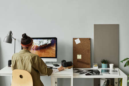 Minimal back view of female photographer editing photos at workplace in studio, copy spaceの写真素材