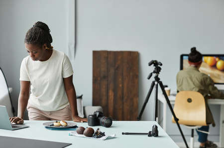 Portrait of young African American woman using laptop while working with food photography in studio, copy spaceの写真素材