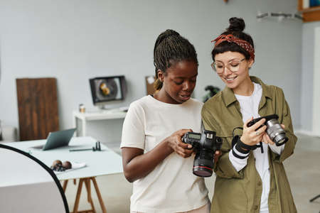 Waist up portrait of two female photographers holding cameras while working in photo studio, copy spaceの写真素材