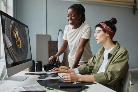 Portrait of two female photographers discussing images on computer screen while working on editing in studioの写真素材