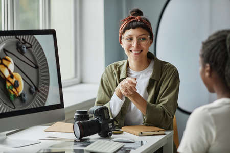Portrait of smiling female photographer collaborating with colleague or client while discussing...