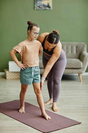 Vertical full length portrait of young girl with down syndrome exercising indoors with female instructor assistingの写真素材