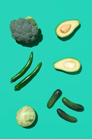 Minimal top view of green vegetables composition on bright blue background, healthy eating and vegan...